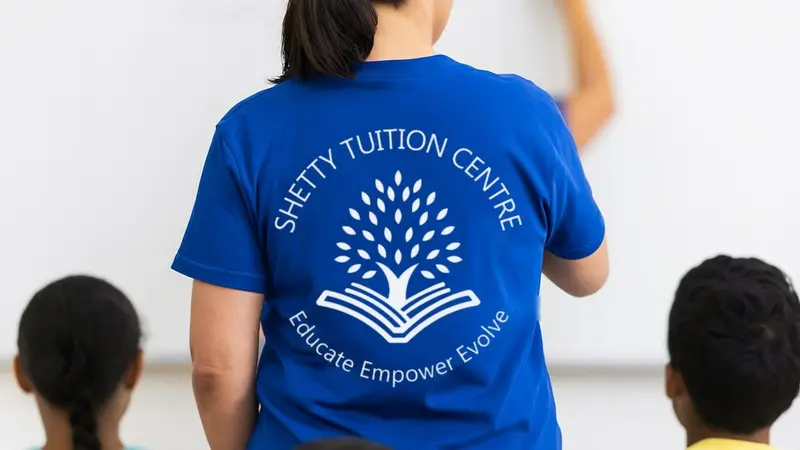A teacher in a blue Shetty Tuition Centre T-shirt writing on a whiteboard, with students watching