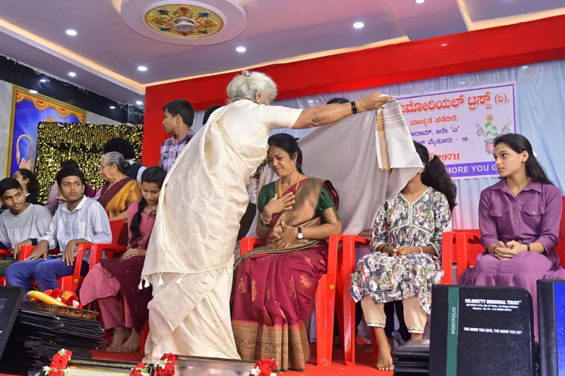Sujatha R Shetty honouring a guest with a shawl on stage at the Annual Donation Event